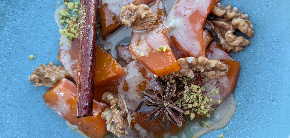 Tabak Tatlisa pumpkin dessert on a blue plate with pumpkins, tahini drizzle, nuts